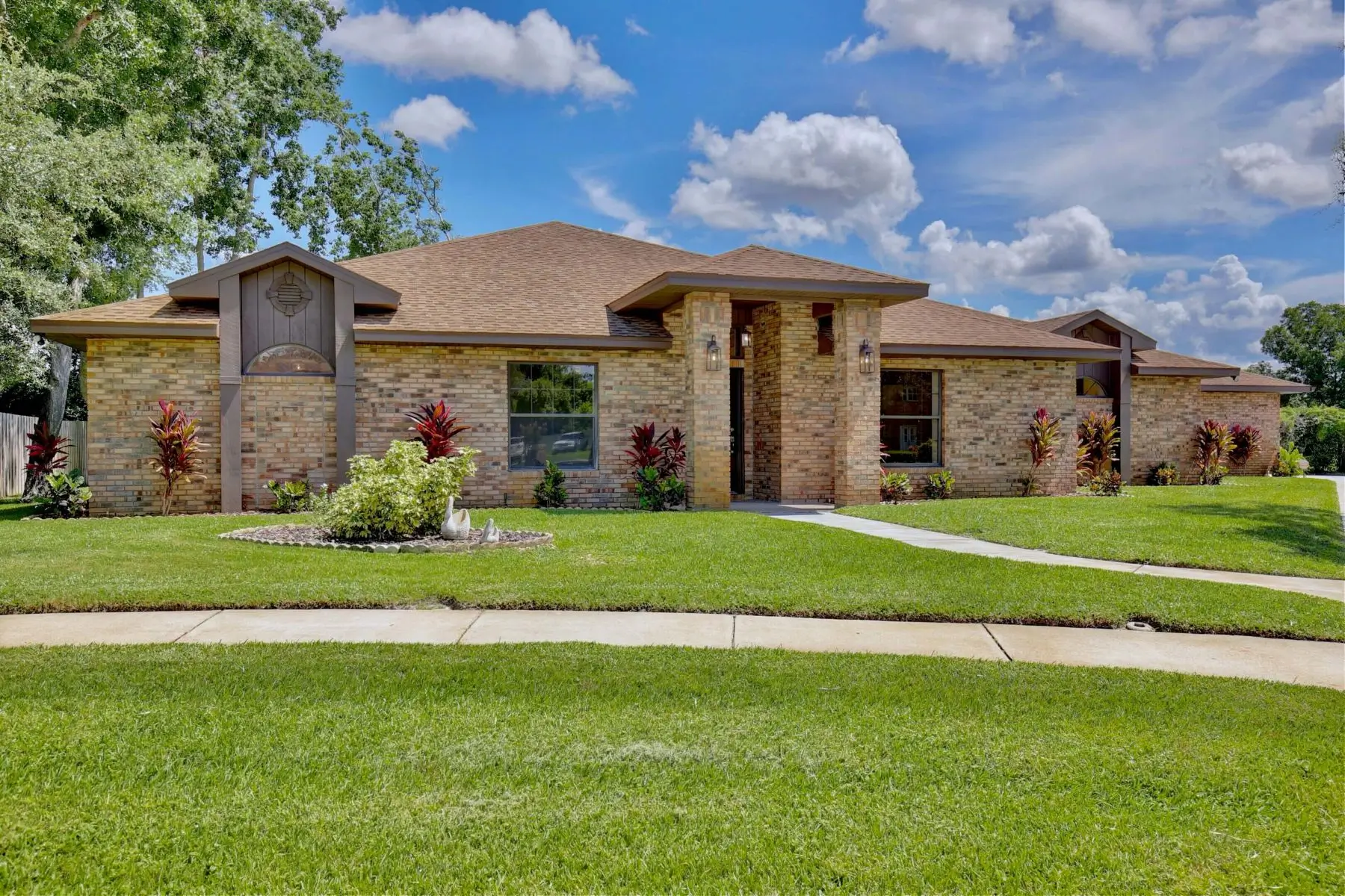 A modern single-story brick house with a well-maintained lawn under a partly cloudy sky.
