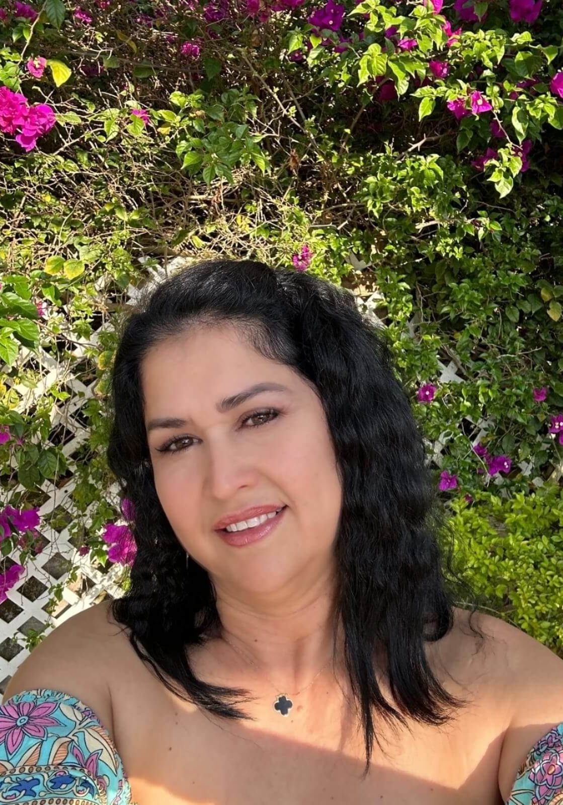 Woman smiling in garden with pink flowers.